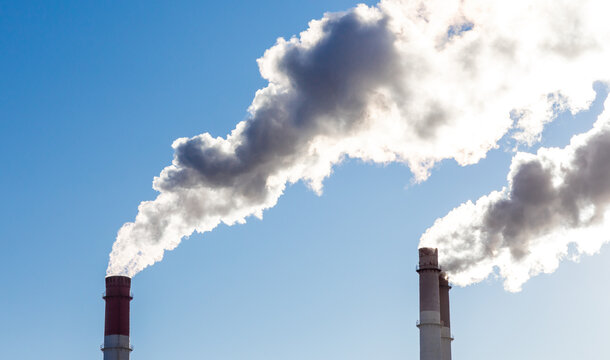 CHP emissions. Smoking chimney releasing smoke against a blue sky. Smoke from factory pipe of heat station in the city. Air pollution. Nuclear power plant cooling. CO2, greenhouse gases emissions.