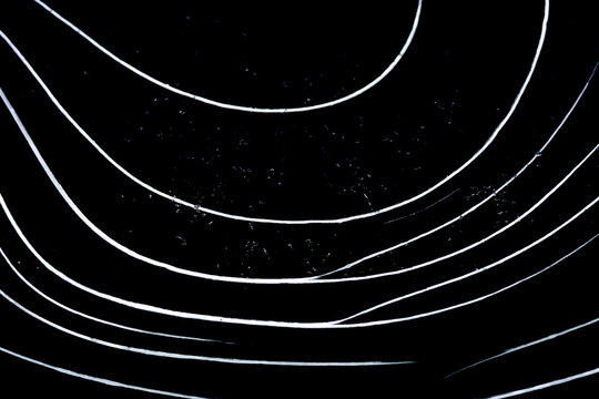 Bright white arcs slice through deep black like chalk on velvet while faint bubbles shimmer within the frozen sheet. The stark scene becomes a bold graphic landscape born of winter quiet