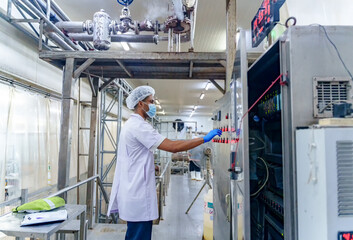 Food processing plant worker in protective gear operates control panel with gloves and mask