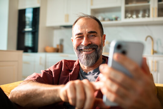 Smiling adult man with braces using smartphone at home kitchen