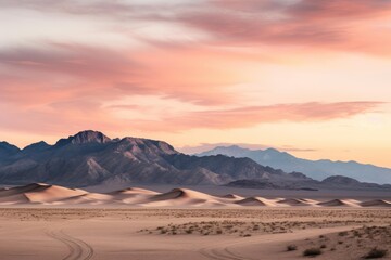 Desert sand dunes stretching towards layered mountains as the sun sets, creating soft light