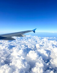 Obraz premium Airplane wing in flight above fluffy white clouds under clear blue sky