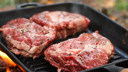 Fototapeta premium Three raw ribeye steaks seasoned with pepper and salt grilling on a cast iron pan