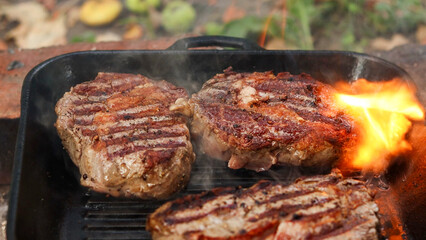 Juicy steaks sizzling and flaring up in a cast iron grill pan outdoors