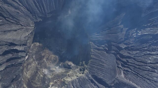 Top view drone footage of Mount Bromo volcanic crater emitting smoke