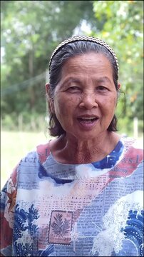 Smiling old asian woman outdoor portrait senior female casual clothing nature background warm expression rural lifestyle daytime light peaceful