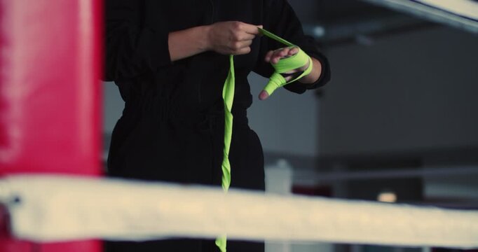 Cropped 4k footage of a young fighter wraps her hands with care and concentration, ensuring her wrists and knuckles are protected for an intense boxing session ahead.. Slow motion video.