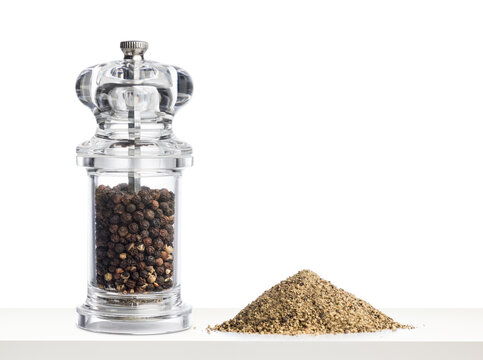 Glass pepper grinder filled with black peppercorns and pepper ground on white table.