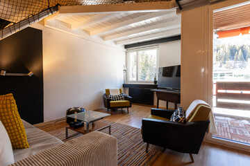 Fototapeta premium Living room with sofa, two armchairs, and cushions. There's a small balcony overlooking the Swiss mountains. Interior of a mountain chalet.