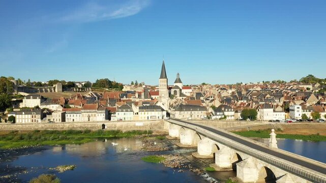 Aerial view of the picturesque town of La Charite sur Loire with its iconic church, historic bridge, and traditional French architecture along the Loire River under a clear blue sky.
