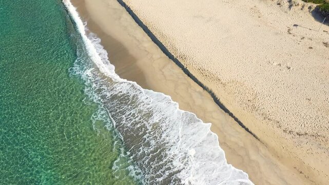 Drone shot of crystal clear turquoise waves gently washing onto the sandy shore of Palinuro beach in Italy. Peaceful coastal landscape with vibrant water and untouched sand.