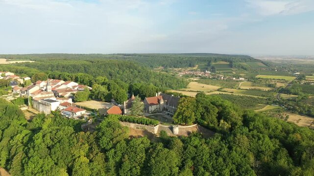 Drone shot of Hattonchatel village surrounded by lush forests and rolling farmland under a clear sky in rural France.