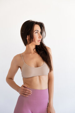 Brunette 30s caucasian Woman in sports bra and leggings poses in studio looking away isolated on white background. Healthy lifestyle. Sexy fit famele body. Workout Clothes. Fitness style. Big breasts.