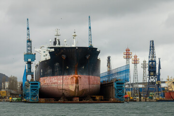 Fototapeta premium A massive tanker vessel with a bulbous bowin in dry dock for maintenance at a commercial shipyard. Shipbuilding, Repair and Maritime industry concept.