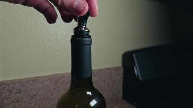 Hand inserting a metal stopper into a wine bottle