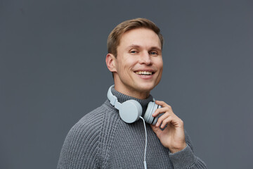 Smiling man with headphones wearing gray sweater isolated on plain gray background studio portrait....