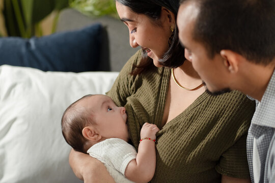 Mother breastfeeding baby with father looking on