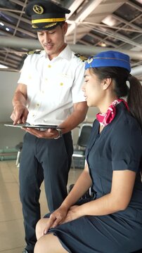 The flight attendants, carrying luggage, and the pilots, all wearing airline business team uniforms, prepare for transportation services, chatting and checking flight schedules on tablets on board the