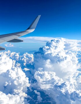 Aerial view of plane wing soaring through fluffy, white clouds against blue sky