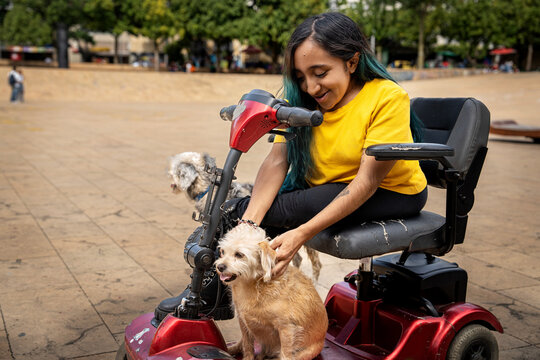 Woman with osteogenesis imperfecta and Dwarfism using an electric wheelchair in a public park accompanied by a dog
