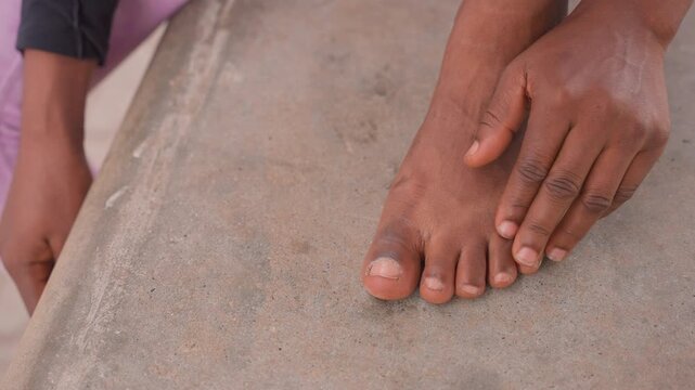 wide black foot on ledge being smoothed and stretched before movement, careful hand adjusting toes, sandy residue on concrete, focused preparation for rehearsal or performance, determined energy