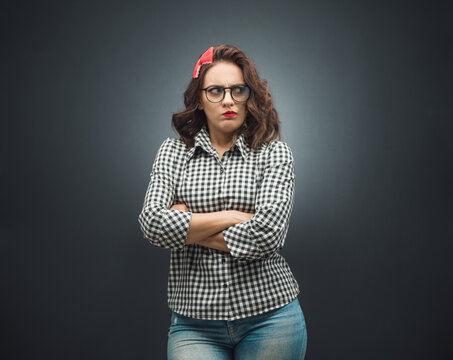Annoyed young woman over dark gray - black background. Displeased girl with arms crossed.