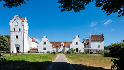 Symmetric exterior view of a historic white church and manor complex framed by dark tree shadows on a sunny summer day
