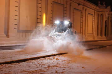 A tractor with a brush clears the road from snow. Repair, cleaning of roads in winter. City improvement services in the cold season. A snowplow cleans the sidewalks. A snowplow clears streets of snow.