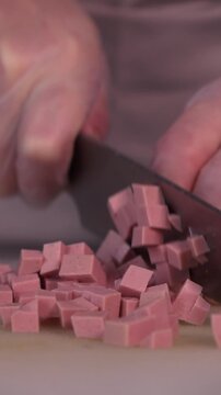 The cook cuts the sausage for the salad. Preparation of appetizers and salads