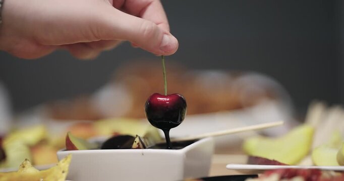 Dipping cherry into dark premium liquid chocolate, slow motion isolated cinematic shot