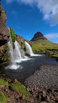 Kirkjufell mountain waterfall under a clear blue sky in iceland with green grass