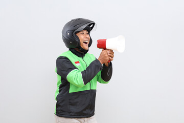 Fototapeta premium Asian online motorbike taxi driver man speaking facing sideways using megaphone giving announcement, news or advertising promotion, isolated on grey background.