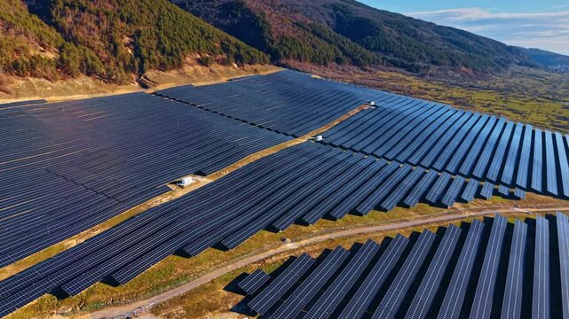 Rows of solar panels on hillside for renewable energy. High angle view of parallel solar panel rows on a grassy mountain slope.