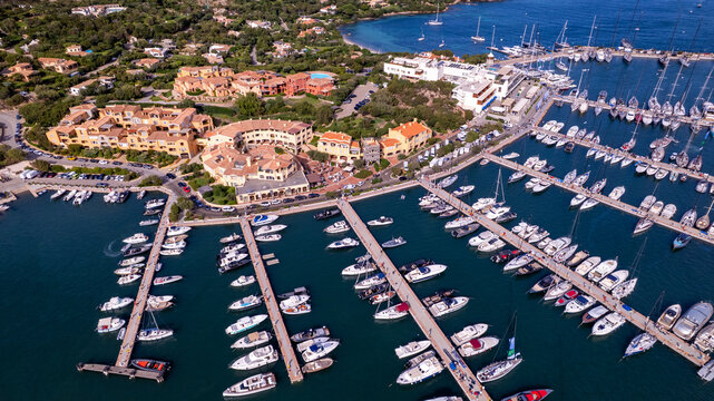 Luxury yachting lifestyle in Porto Cervo marina aerial drone view . Expensive speedboats and sailing ships in turquoise bay. Wealthy summer vacation in Italy