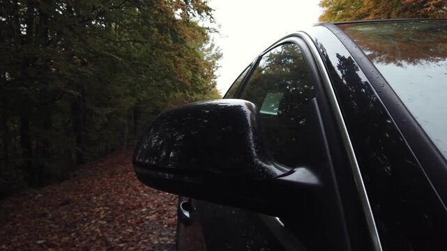 Broken black passenger car with engine failure and emergency flashing light is parked on side of mountain rural road in forest waiting for tow service