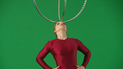 Young circus gymnast in a red leotard standing on a green background and holding the hoop on her forehead. For acrobatics, circus show and chroma key video production. © kinomaster