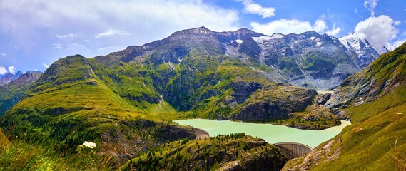 Naklejka premium Panoramic view at Pasterze Glacier Grossglockner Lake dam among austrian Alps mountains summits blue sky clouds.