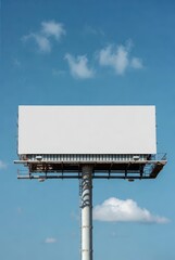 Obraz premium Large blank outdoor billboard mockup on metal pole against clear blue sky with white clouds, horizontal city street advertising hoarding display for commercial marketing presentation