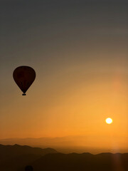 Naklejka premium Single Hot Air Balloon Silhouette a Vibrant Orange Sunrise Sky in Morocco