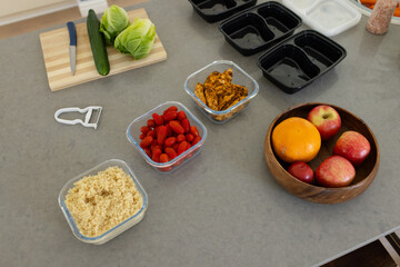 Clear glass containers are holding grain, tomatoes, and chicken on gray countertop, with fruit bowl