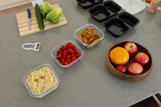 Clear glass containers are holding grain, tomatoes, and chicken on gray countertop, with fruit bowl