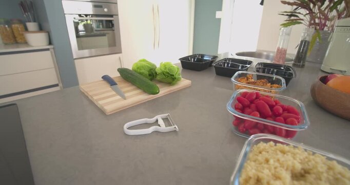 Camera is pushing forward across countertop, revealing cucumber, tomatoes, grains, documenting prep