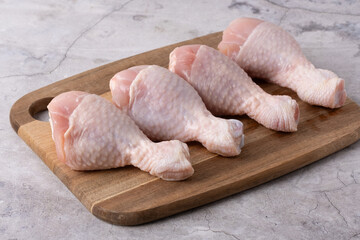 Fresh chicken drumsticks arranged on a wooden cutting board ready for cooking in a kitchen setting