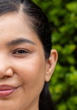 Mid adult woman posing for close-up portrait outdoors at green hedge, showing facial texture