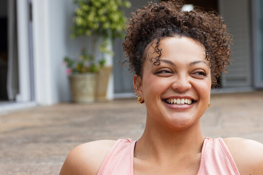 African American woman smiling looking left at patio planter wearing pink tank top and gold hoops