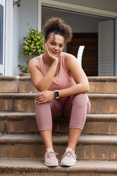 African American woman sitting on stone front porch steps, wearing pink activewear, smartwatch
