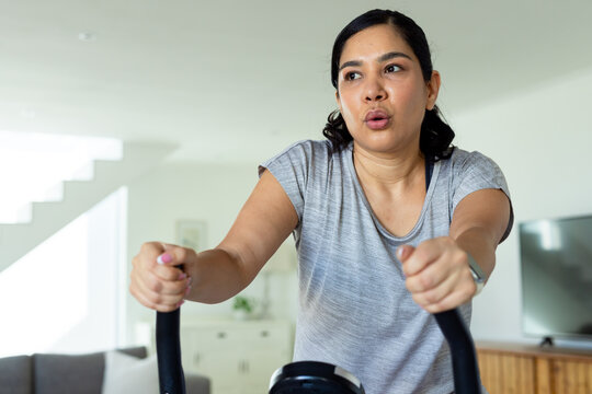 Woman pedaling on stationary bike wearing grey T-shirt and smartwatch in living room