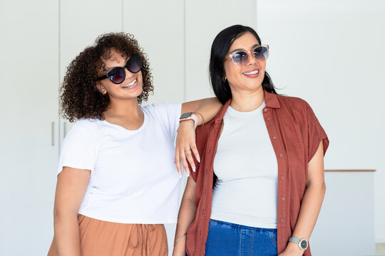 Diverse female friends standing in bright home kitchen wearing sunglasses and wristwatch