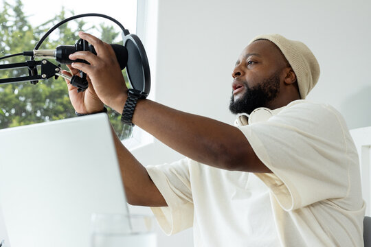 African American man adjusting condenser microphone with pop filter at home studio desk with laptop