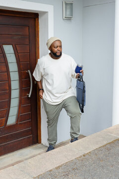 African man stepping out onto front step wearing beanie olive joggers holding tumbler and tote